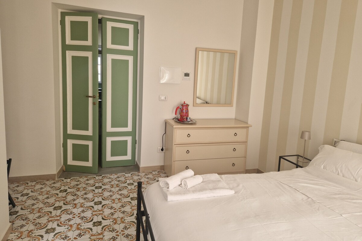A hotel room with a bed, a dresser, a mirror, and a green door.