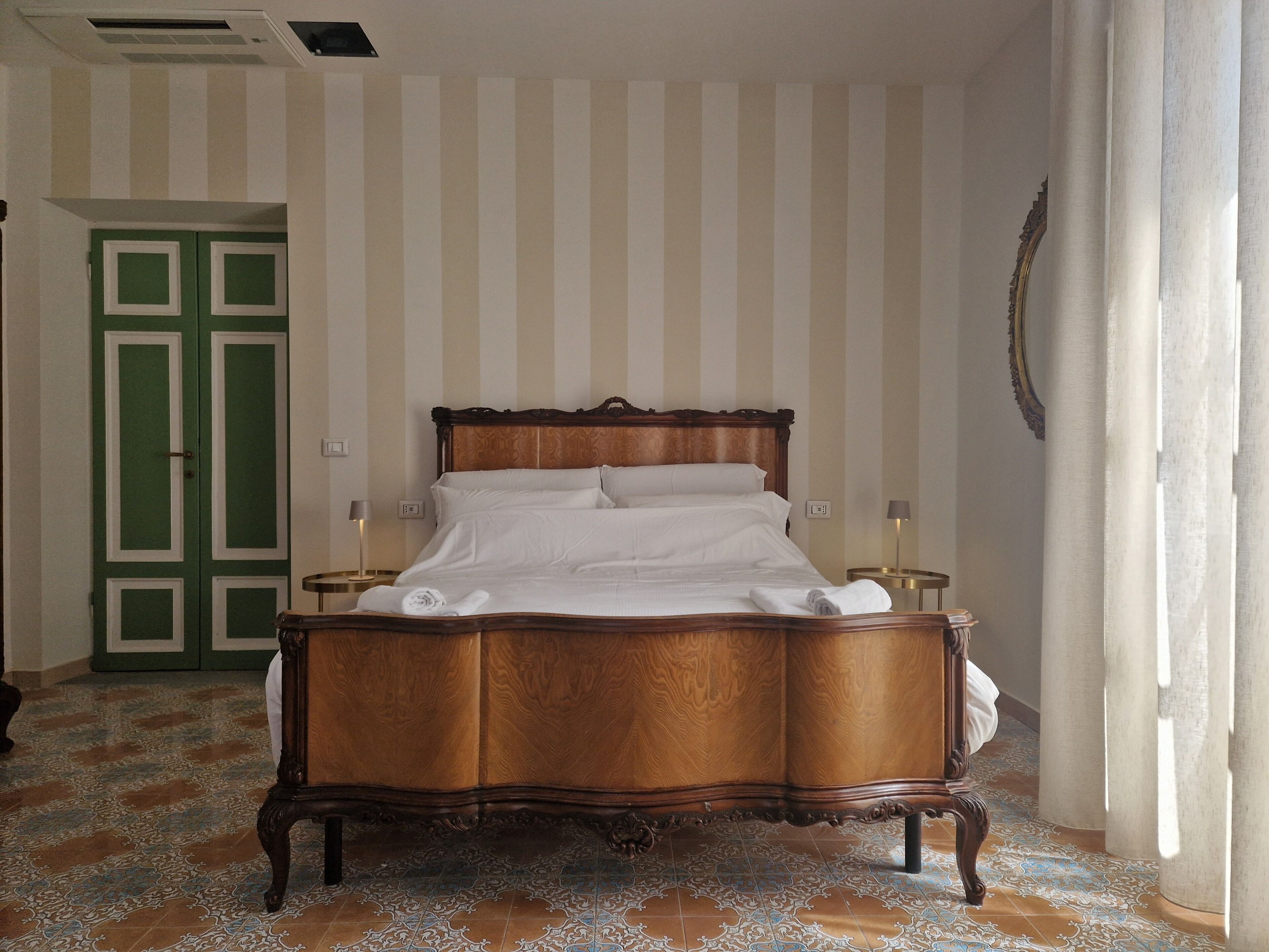 A hotel room with a large bed, two bedside tables, a green door, and striped wallpaper.