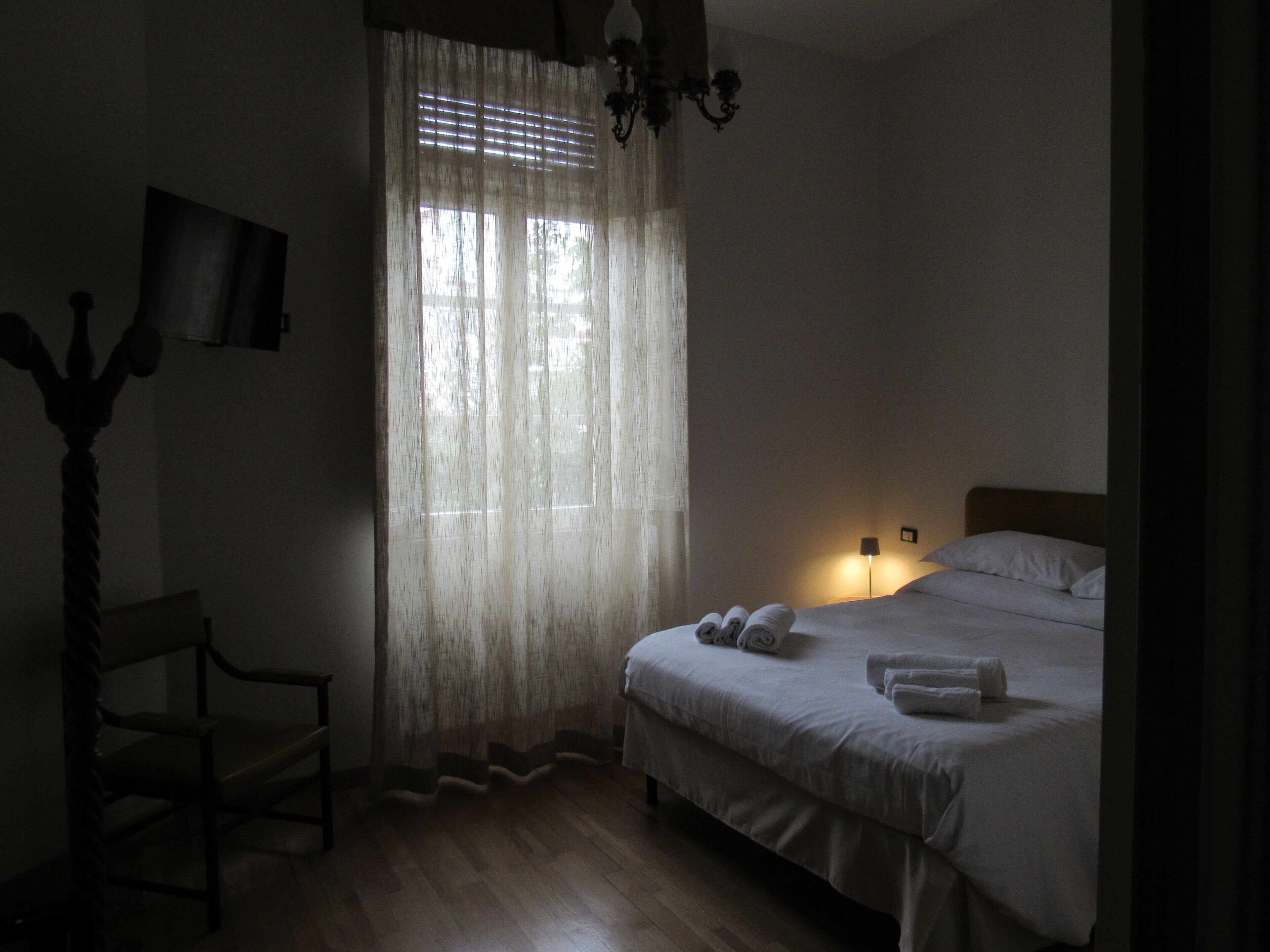 A dimly lit room with a bed, a chair, a lamp, and a window with curtains.