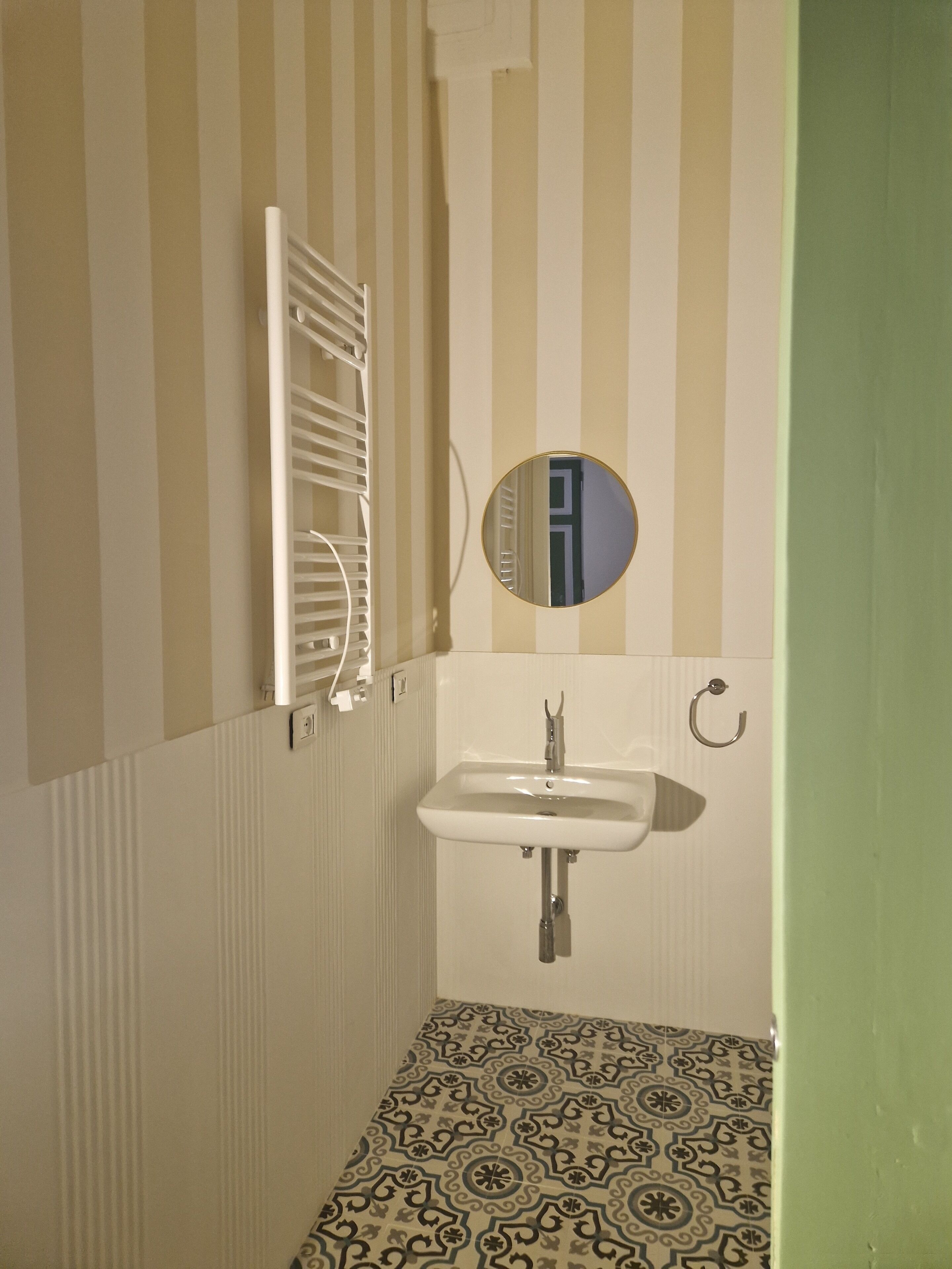 Une salle de bain avec un mur à rayures, un lavabo blanc, un miroir et un sol à motifs.