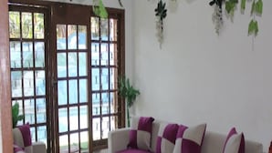 Sala de estar com sofá, mesa de centro e uma cadeira. Janelas oferecem vista do céu azul e do verde.