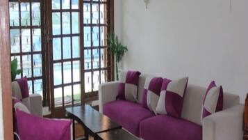 A living room with a sofa, a coffee table, and a chair. There are windows with a view of a blue sky and greenery.