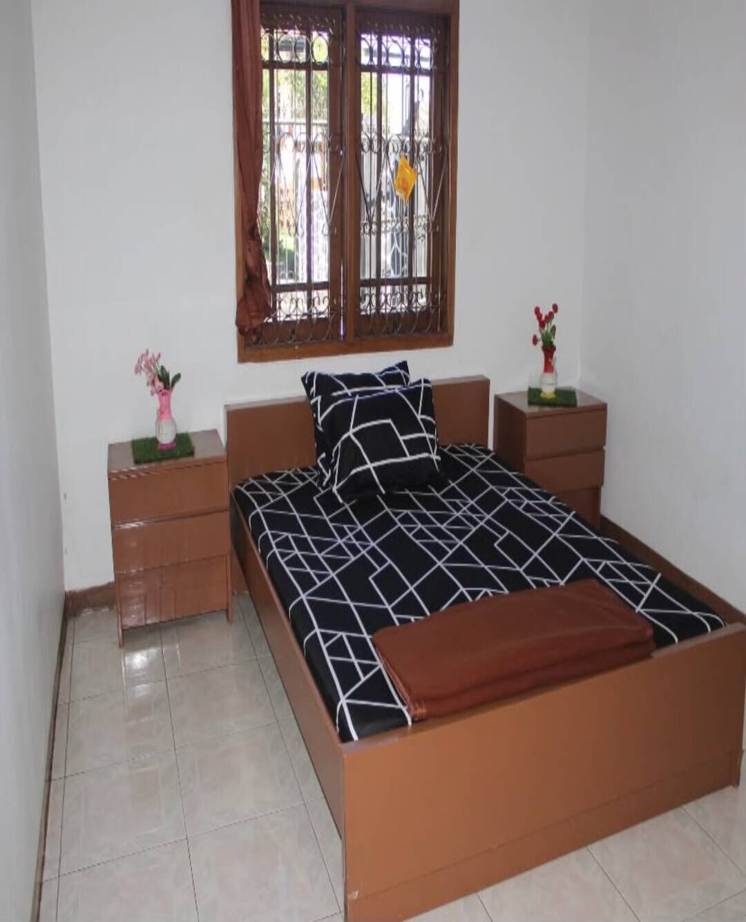 A bedroom with a bed, two nightstands, a window with curtains, and a small table with a vase.
