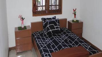 A bedroom with a bed, two nightstands, a window with curtains, and a small table with a vase.