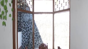 Quarto com cama de canto, mesa de jantar e vista pela janela com padrão de pedra.