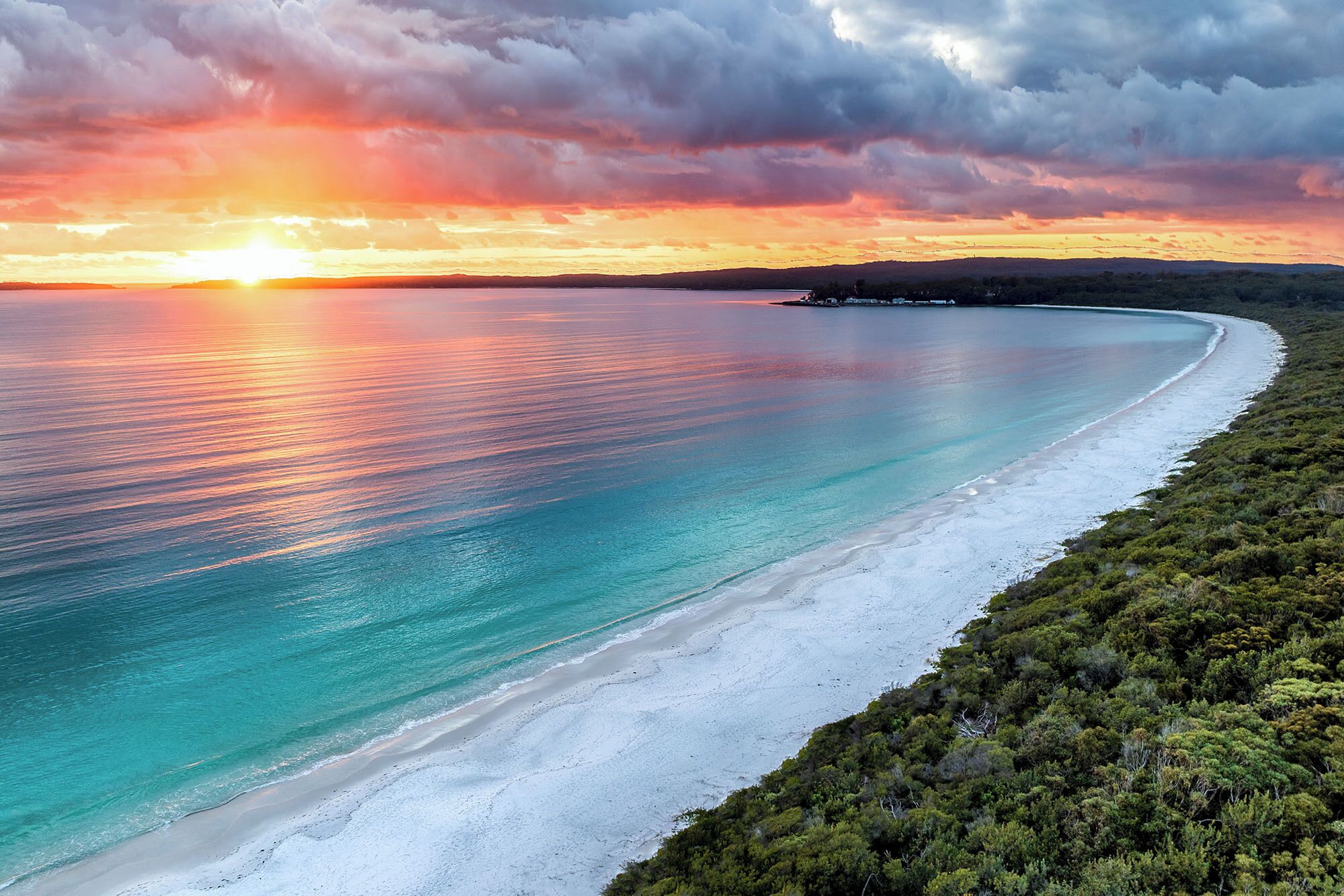A coastal landscape with a beach, clear water, and a sunset.