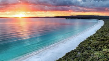 A coastal landscape with a beach, clear water, and a sunset.