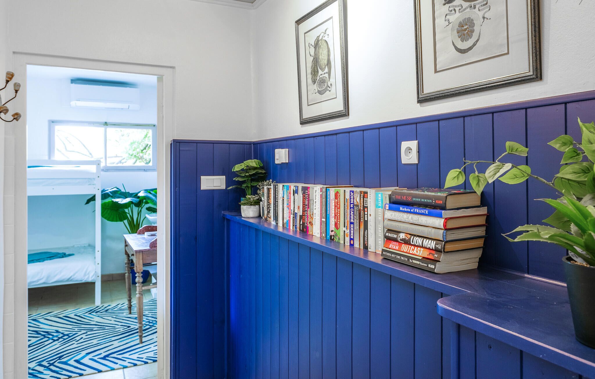 Ein Flur mit blauer Wand, einem Bücherregal mit Büchern, einer Topfpflanze und gerahmten Bildern an der Wand.