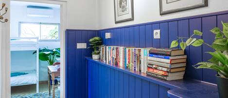 Ein Flur mit blauer Wand, einem Bücherregal mit Büchern, einer Topfpflanze und gerahmten Bildern an der Wand.