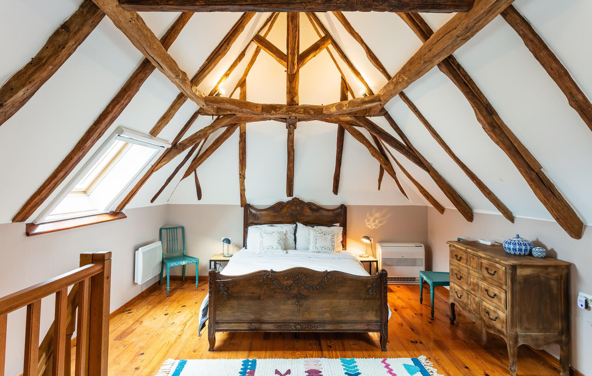 A bedroom with a sloped ceiling, a wooden bed, a dresser, and a radiator.