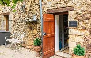 A rustic stone building with a wooden door, a metal chair, and a small shelf with a lantern. - Gorgeous home in Montferrand-du-Périgor (Montferrand-du-Périgor)
