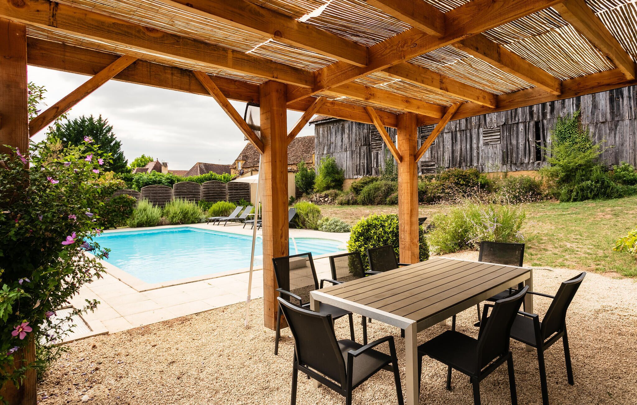 A covered outdoor area with a pool, a table with chairs, and a wooden fence in the background.