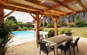 A covered outdoor area with a pool, a table with chairs, and a wooden fence in the background. - Gorgeous home in Montferrand-du-Périgor (Montferrand-du-Périgor)