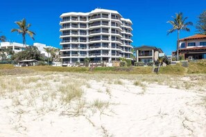 Ein mehrstöckiges Hotel mit Balkonen in der Nähe eines Strandes mit Dünen und Palmen.