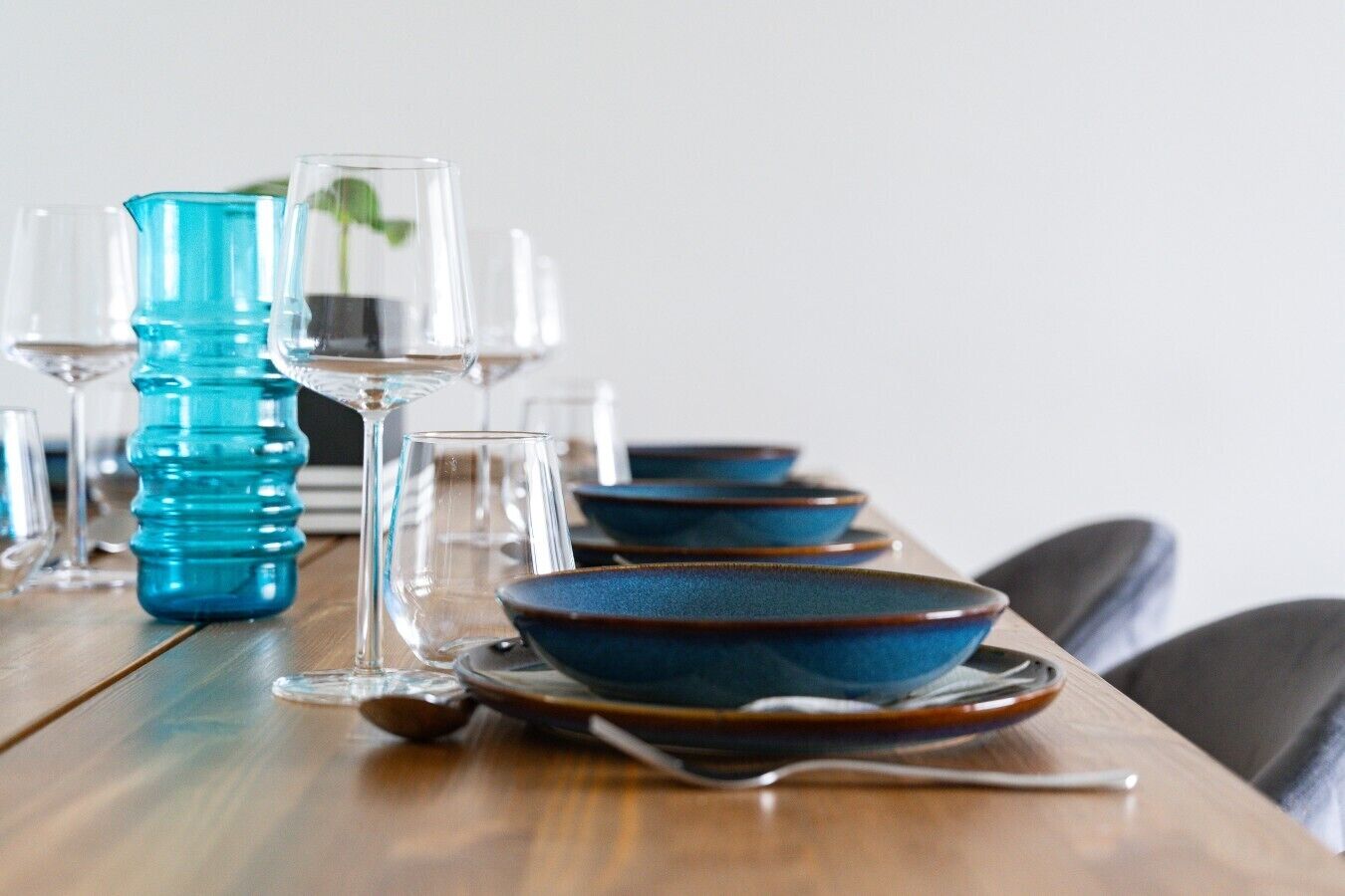 Mesa de jantar posta com tigelas azuis, copos transparentes e uma garrafa de água azul.