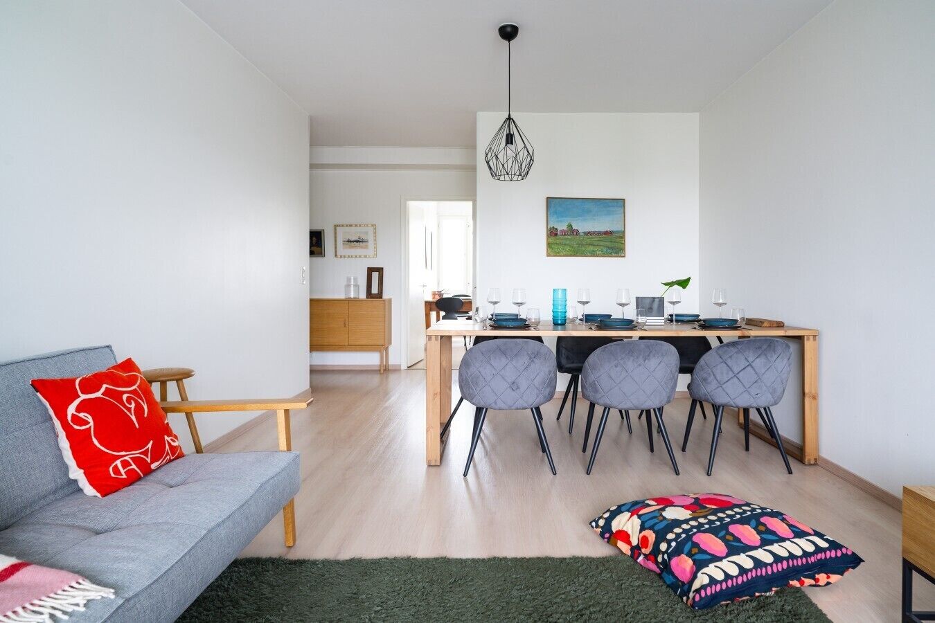 Un salon moderne avec un canapé gris, un tapis coloré et un coin repas comprenant une table et des chaises en bois.