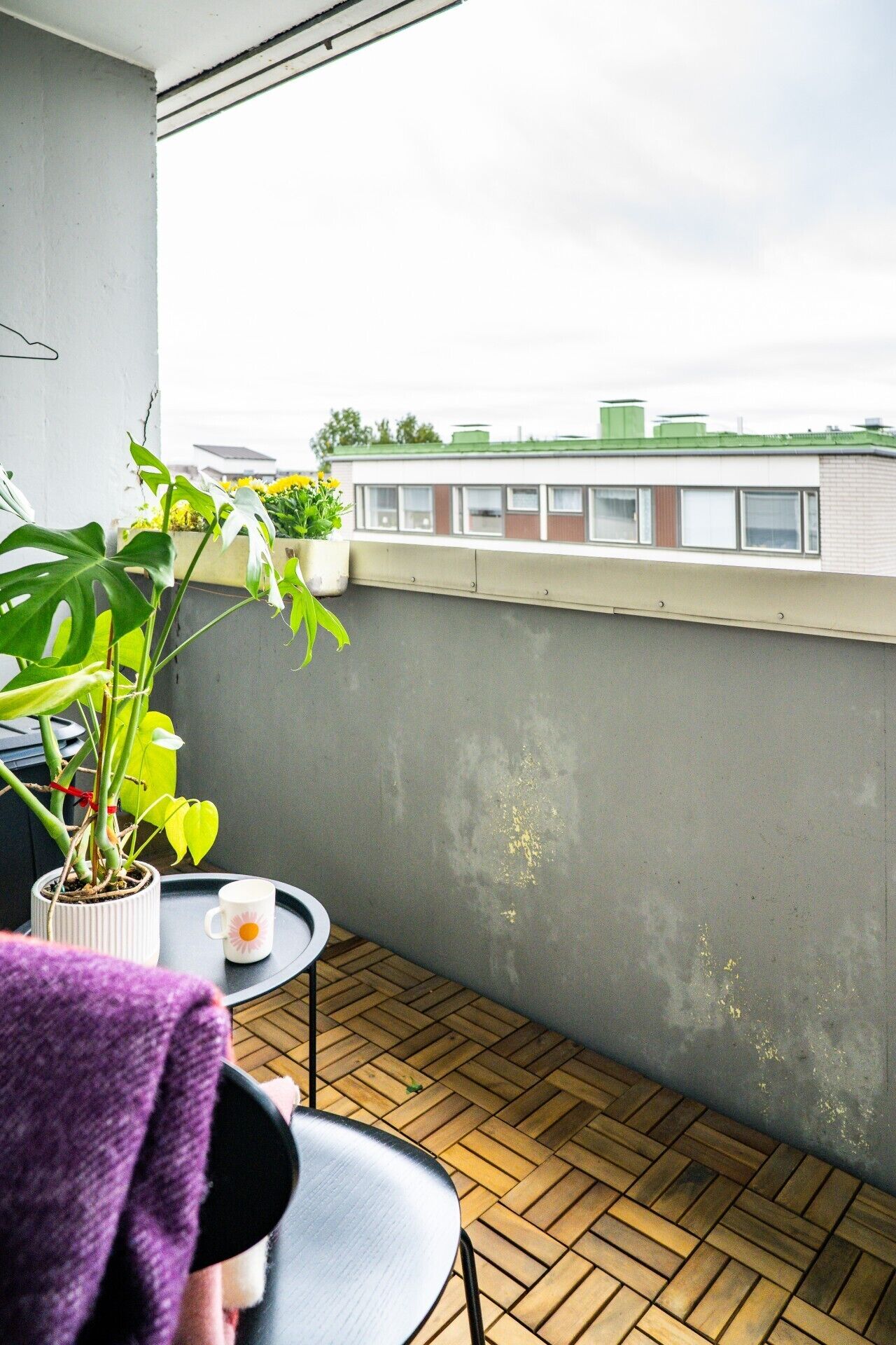 A balcony with a potted plant, a small table with a cup, and a chair.