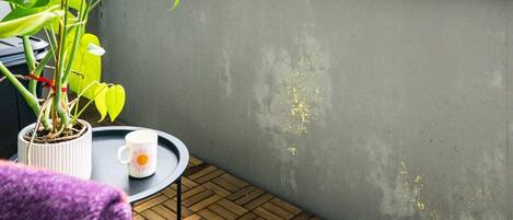 A balcony with a potted plant, a small table with a cup, and a chair.