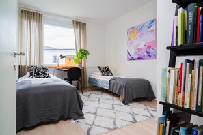Ett hotellrum med två sängar, ett skrivbord, en bokhylla och ett fönster med gardiner.