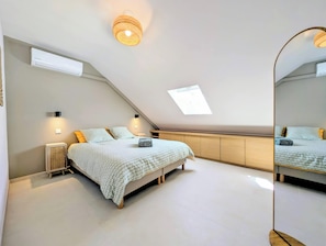 Un dormitorio con techo inclinado, una cama con ropa de cama estampada, una mesita de noche, un aire acondicionado montado en la pared y un aplique de techo.