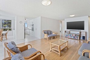 A modern living room with a flat-screen TV, wicker furniture, and a bookshelf. - Ambassador Beachfront Burleigh Heads (Gold Coast)