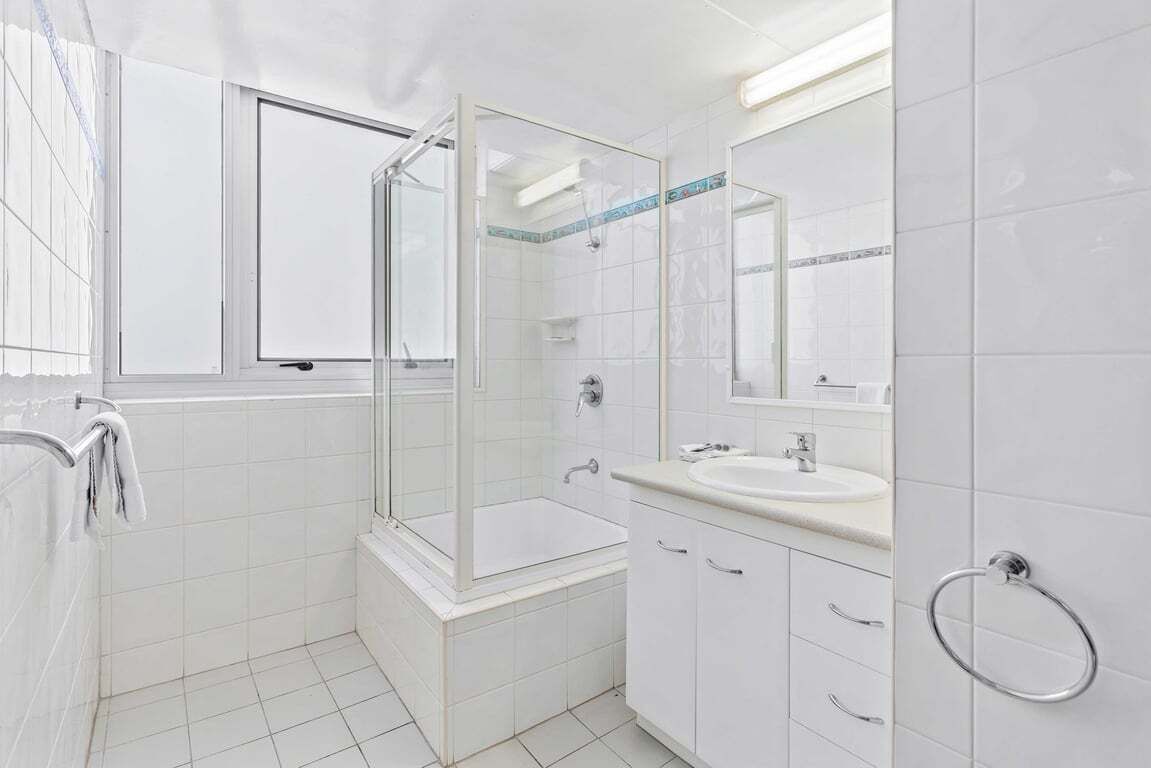 A bathroom with a glass-enclosed shower, a sink, and a mirror.