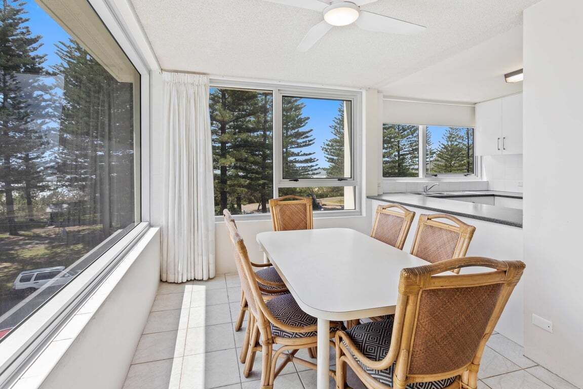 A dining area with a table and chairs, large windows with a view of trees, and a ceiling fan.