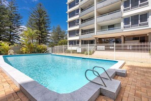 A swimming pool with a metal ladder, surrounded by a brick patio, and a multi-story building with balconies in the background. - Ambassador Beachfront Burleigh Heads (Gold Coast)