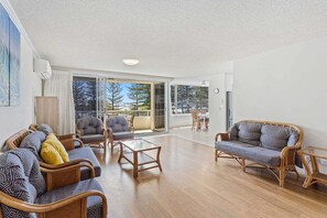 A spacious living area with a large sliding glass door leading to a balcony, furnished with wicker sofas and armchairs. - Ambassador Beachfront Burleigh Heads (Gold Coast)