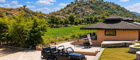 A black off-road vehicle parked in a paved area with a building featuring a tiled roof and a stone wall.