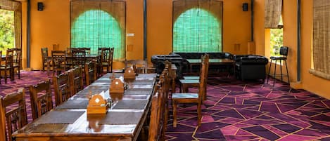 Un espacio de comedor techado con mesas, sillas y un sofá, además de una alfombra estampada.