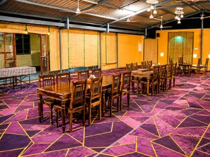Un salón de conferencias con varias mesas y sillas, una alfombra estampada y ventiladores de techo.