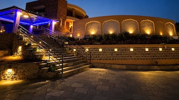 Un edificio con fachada curva, una escalera que conduce a un nivel superior y una serie de elementos decorativos iluminados en la pared.