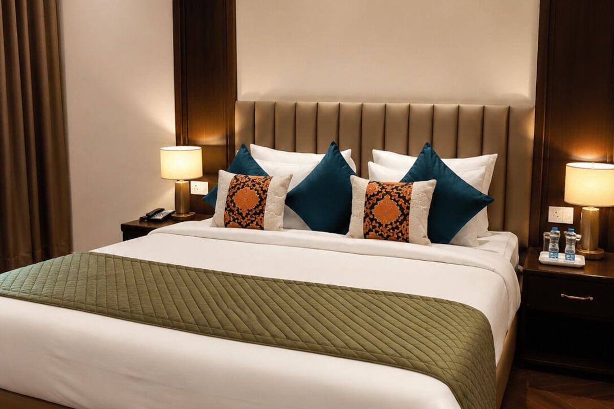 A hotel room with a large bed, two bedside tables, and a headboard with built-in lighting.