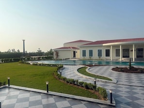 A modern building with a pool, surrounded by a well-maintained lawn and a checkered pathway.