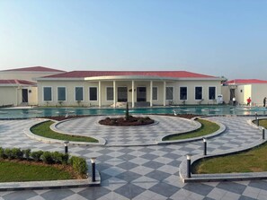 A hotel with a pool, a checkered walkway, and a covered area with columns. - Moksha Resort and Spa  (Kapur Pind)