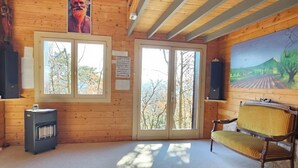 Quarto com paredes de madeira e uma janela grande, um banco e um aquecedor.