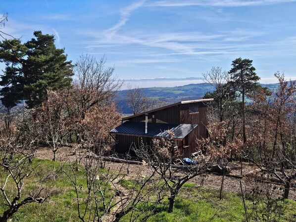 Een rustieke blokhut met een schuin dak, omgeven door bomen en een helder uitzicht op verre bergen.