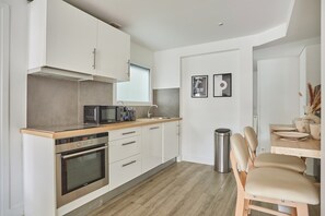A modern kitchen with a built-in oven, microwave, and toaster, wooden countertop, and a dining area with a table and chairs. - Superbe Apartment Arc de Triomphe/champs Elysees (Paris)