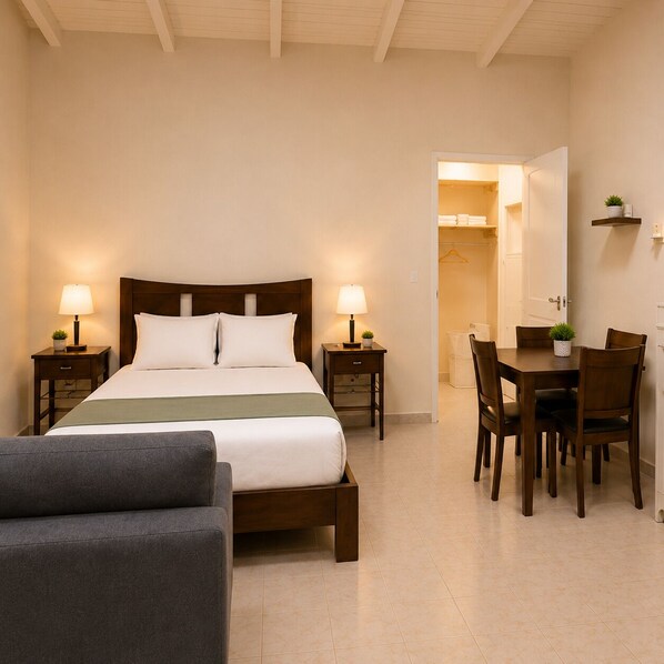 A hotel room with a bed, bedside tables, a desk with chairs, and a small table with a plant. - Cozy Curaçao Studio for 4 with AC & Private Patio (willemstad)
