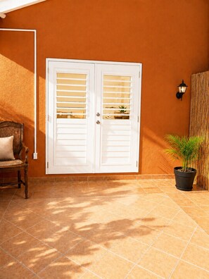 A patio with a white door, a wicker chair, a potted plant, and a wall-mounted light fixture. - Cozy Curaçao Studio for 4 with AC & Private Patio (willemstad)