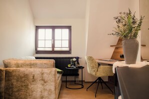 A cozy living room with a sofa, a chair, a small table with a vase of flowers, and a radiator.