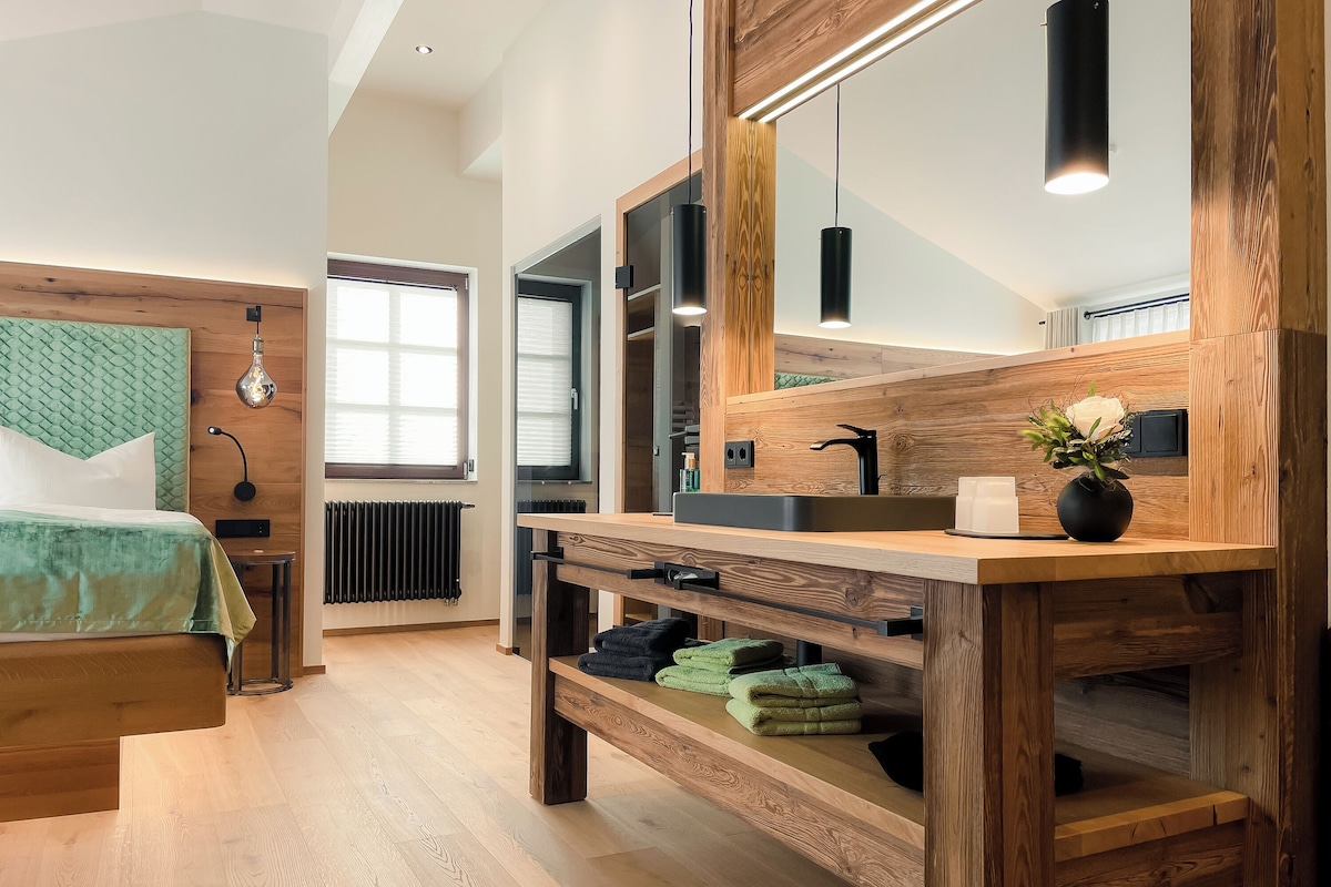 A modern bathroom with a wooden vanity, a large mirror, and a green towel rack.