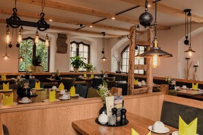 A restaurant interior with wooden benches, hanging pendant lights, and a central wooden structure. - Altstadt-Hotel Freiberg - Wellness (Freiberg)