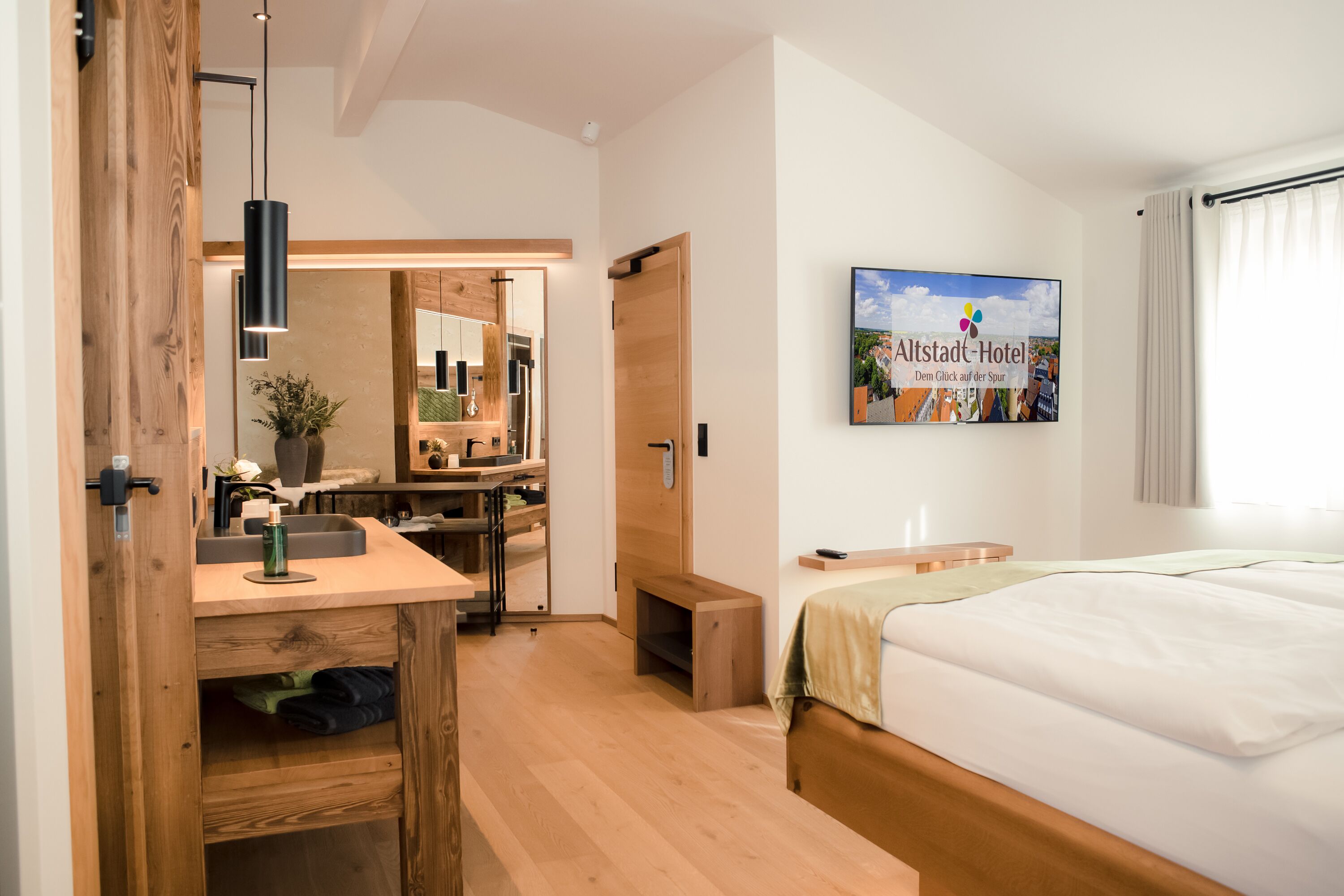 A hotel room with a wooden desk, a bed, a large mirror, and a wall-mounted TV.