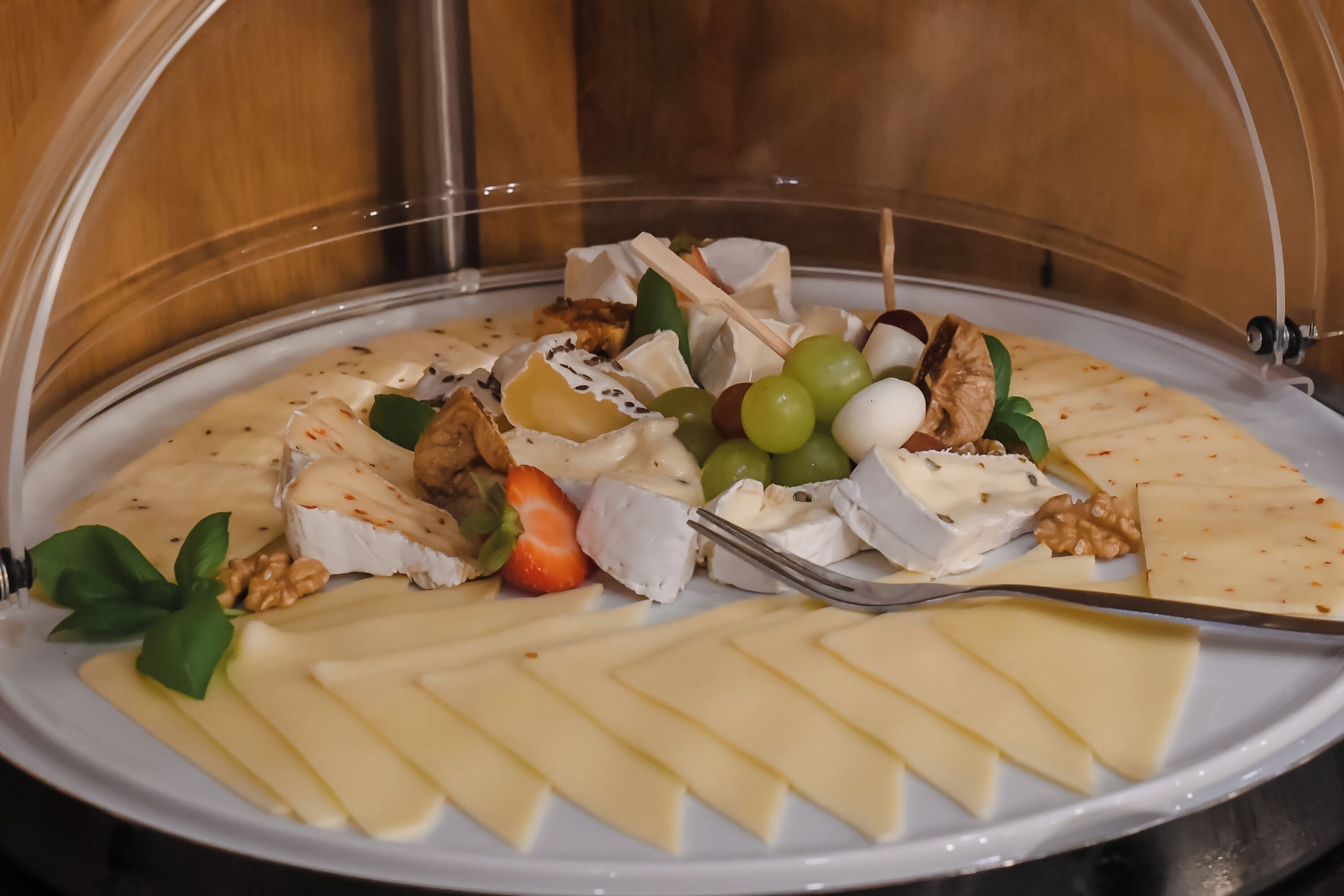 Una tabla de quesos con diferentes tipos de queso, uvas, nueces y una fresa, servida en un plato blanco.