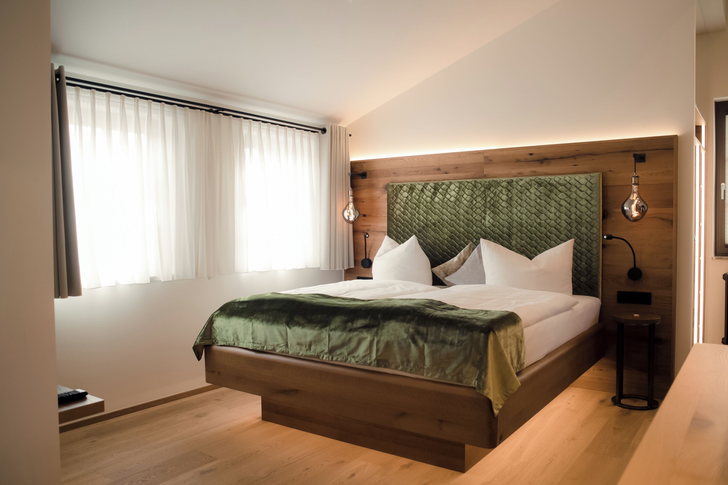 Ein modernes Schlafzimmer mit einem Holzkopfteil, einem großen Bett, einem Nachttisch und einem Fenster mit Vorhängen.