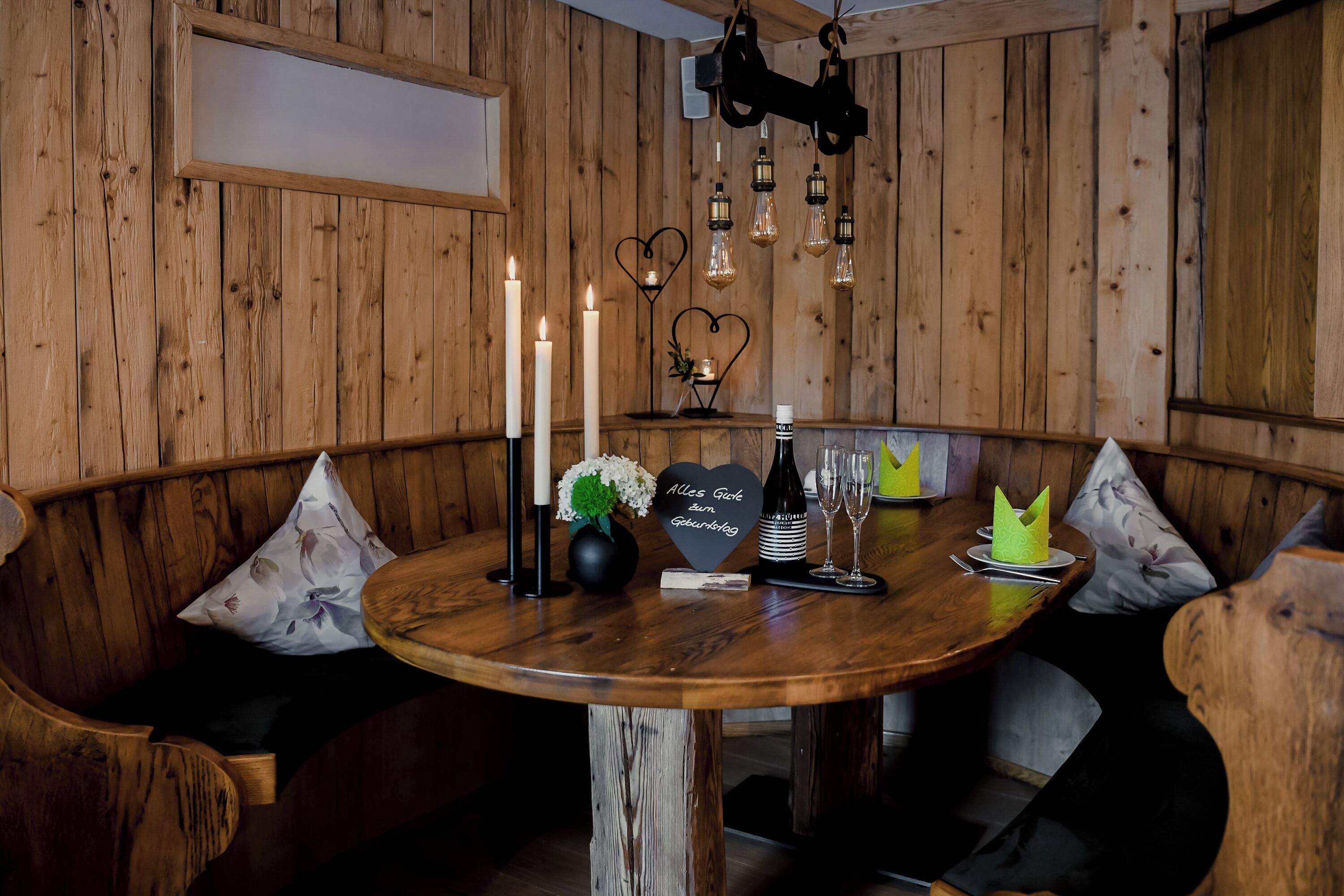 Een houten interieur met een ronde tafel, kaarsen, een fles, glazen en decoraties in de vorm van harten.