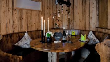 Een houten interieur met een ronde tafel, kaarsen, een fles, glazen en decoraties in de vorm van harten.