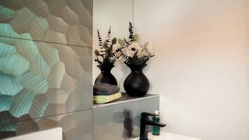 Une salle de bain au design moderne, dotée d’un grand miroir, d’un lavabo blanc et de deux vases noirs ornés de fleurs.